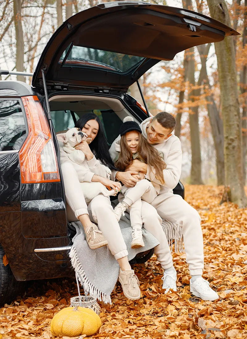 Mietwagen leihen Muhr Autoverleih - Eltern mit Kind sitzen im Kofferraum eines Wagens, der in einem herbstlichen Wald geparkt wird