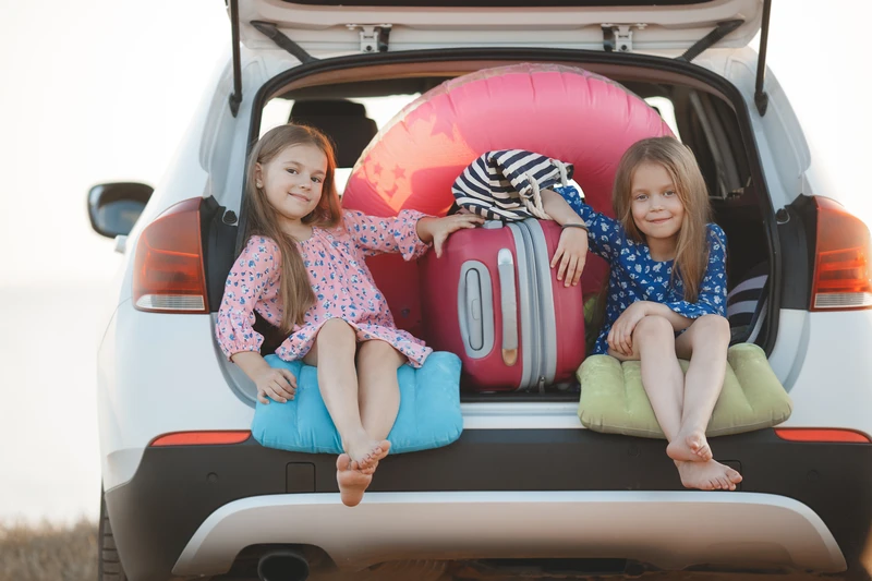 Wochenendurlaub mit der Familie - Zwei Mädchen sitzen im Kofferraum eines Autos