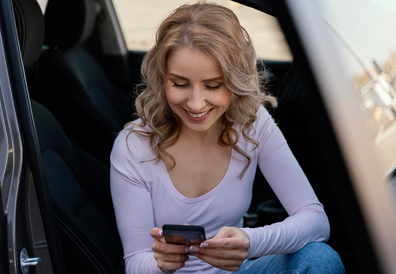 E-Auto Apps - Frau sitzt in einem Auto und guckt auf ihr Smartphone