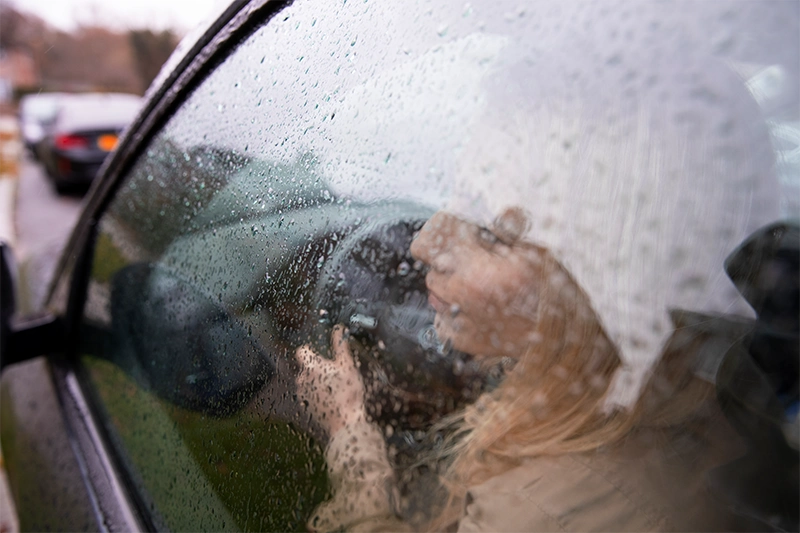 Aquaplaning Mietwagen - Frau sitzt im Auto hinter einer nassen Fensterscheibe